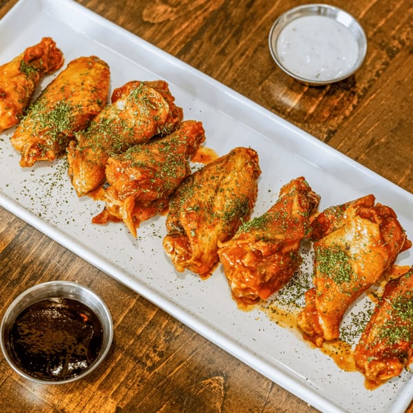 A white rectangular platter of HWY 47 KITCHEN's chicken wings with two dipping sauces.