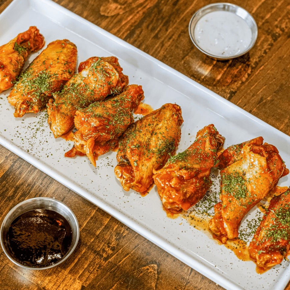A white rectangular platter of HWY 47 KITCHEN's chicken wings with two dipping sauces.
