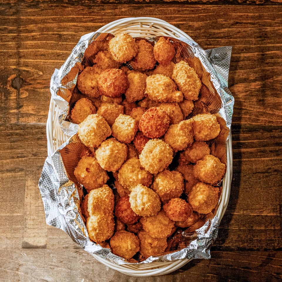 A white basket filled with golden-brown, breaded fried cheese curds on a wooden table.