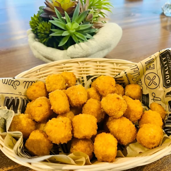 A white wicker basket filled with golden-brown fried cheese curds, lined with patterned paper.