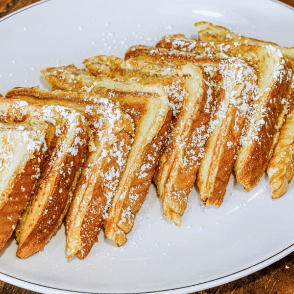 Golden-brown French toast slices, dusted with powdered sugar, arranged on a white plate.
