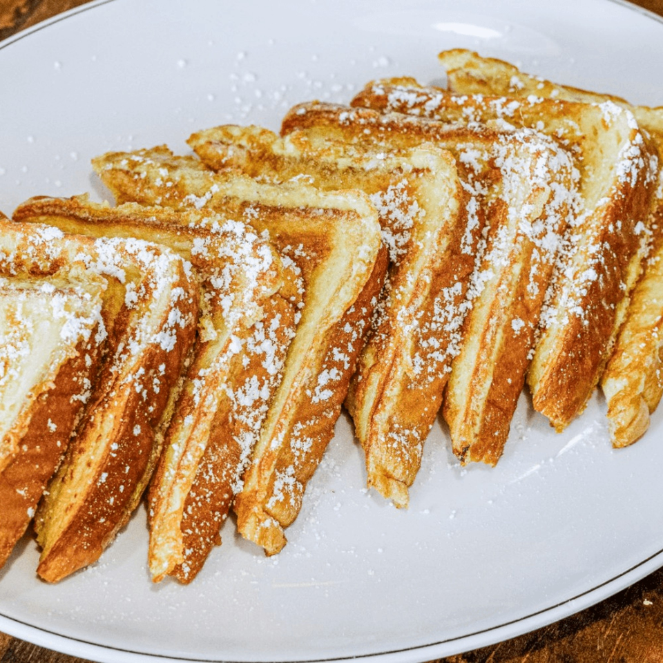 Golden-brown French toast slices, dusted with powdered sugar, arranged on a white plate.
